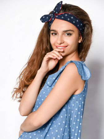 Cute young curly girl in a polka dot denim summer dress looking playfully at the camera. . Cute girl in romantic clothes is going on a date, smiling pretty on a white background.の写真素材