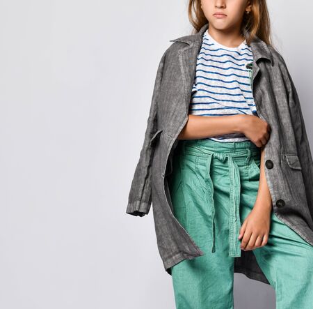 Cropped photo of a teenage girl in stylish wide pants and a linen trench coat looking at the camera and smiling, standing against a white wallの写真素材