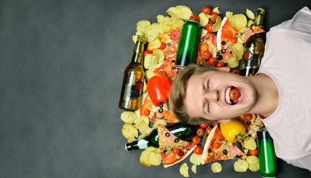 young man lies surrounded by pieces of pizza. chips bottles with alcohol and beer. Morning after...