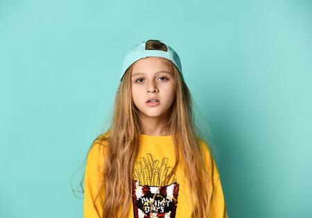 positive young female wearing orange hoody and baseball cap posing on a blue backgroundの写真素材