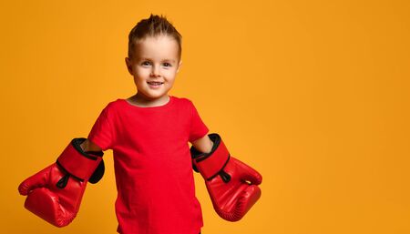 Little Cute Boy 4 years old in a red T-shirt and red boxing gloves on a yellow backgroundの写真素材