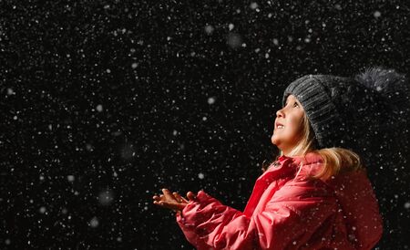Little girl catches snowflakes stretching out her hands forward. A child enjoys playing outdoors....