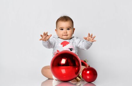 Cute baby girl in grey bodysuit and terry socks plays on the floor with Christmas red ballsの写真素材
