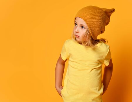 Stylish little girl in hipster hat and yellow T-shirt poses against a bright backgroundの写真素材