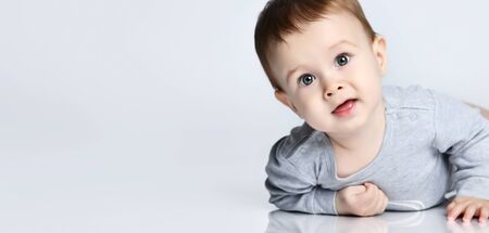 Portrait of little baby boy toddler in grey casual jumpsuit lying on floor and smiling over white...