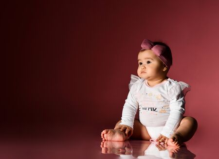 Little kid in a headband and smart white bodysuit with inscription, barefoot. She looking at...