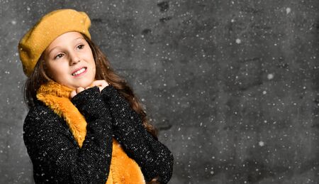 Portrait of young smiling girl model in stylish casual winter clothing and bright yellow accessories over grey concrete wall background with snowflakes. Trendy youth casual winter fashion conceptの写真素材