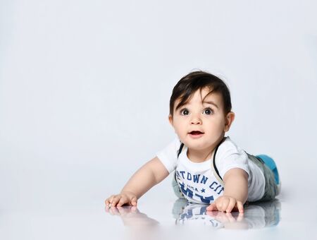 Toddler in t-shirt with inscriptions, jeans with suspenders. He is laying on the floor isolated on...