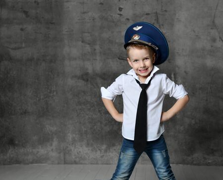 Smiling boy in white shirt, jeans, tie and police cap standing and playing in policeman over grey background. Trendy children clothes and children games conceptの写真素材