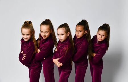 Group of young smiling girls gymnasts in dark red velvet sport costumes standing and posing over white background. Rhytmhic gimnastics beauty and team sport cocneptの写真素材
