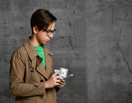 Young teen boy in brown costume and glasses standing and counting dollars over grey concrete wall...