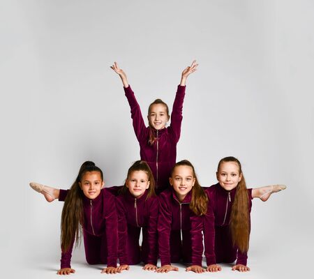 Team of young smiling girls gymnasts in dark red velvet sport costumes posing over white background. Rhytmhic gimnastics beauty and team sport cocneptの写真素材