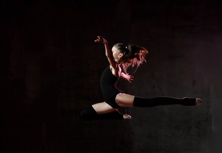 Artistic little girl gymnast in black sport body and special tops high jumping in gymnastic pose...