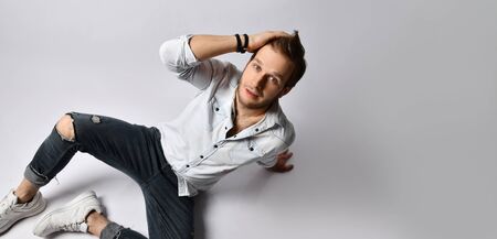 Handsome hipster man in shirt, bracelets, gray holey jeans and sneakers. He is smiling with closed...