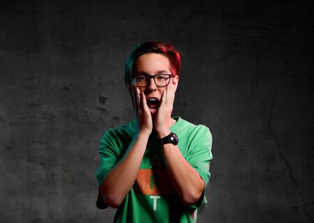 teenager in glasses and a green T-shirt grabbed his head in surprise and heard. Emotions Blimey!