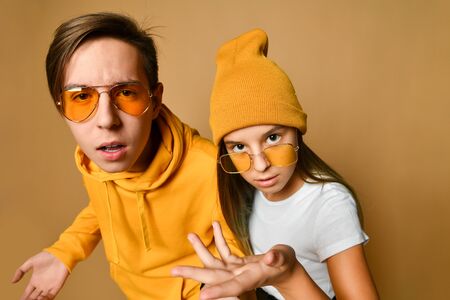 Swag teens boy and girl in comfortable clothing, hats and sunglasses standing and expressing...