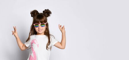 little girl with a big smile, wearing dark glasses in a White Studio. Stands with his hands raised...