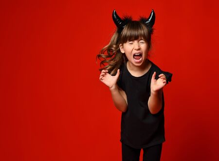 Little brunette kid with devil horns, ponytail, in black blouse and leggings. She is screaming with...
