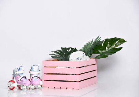 Pink wooden box with flower leaves and hats and roller skates on white studio backgroundの写真素材