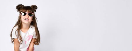 A little smiling girl in sunglasses in a white Studio. In a white t-shirt with a pink Flamingo. Two bunches and loose hair, horns.の写真素材