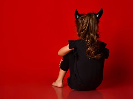 Little brunette child with devil horns, ponytail, dressed up in black blouse and leggings, barefoot....