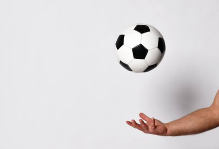Hand of a man with golden wedding ring on his finger is throwing up a soccer ball, isolated on white studio background. Concept of sport, balance and agility. Close up, copy spaceの写真素材