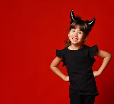 Charming brunette girl with devil horns, ponytail, dressed up in black blouse and leggings. She is...