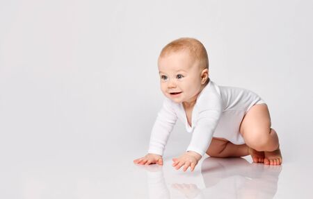Chubby ginger baby boy in bodysuit, barefoot. He smiling, creeping on floor isolated on white studio background. Concept for articles about childhood or advertising for babies. Close up, copy spaceの写真素材