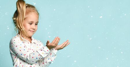 Little kid with ponytail, dressed in shirt with hearts print. She smiling, acting like holding something in her hands, posing on green background. Childhood, fashion, advertising. Close up, copy spaceの写真素材