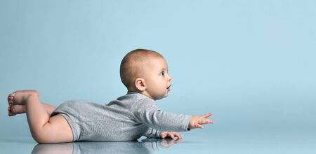 Ginger toddler in gray bodysuit, barefoot. He is sitting on the floor against blue studio background. Concept for articles about childhood or advertising for babies. Close up, copy spaceの写真素材
