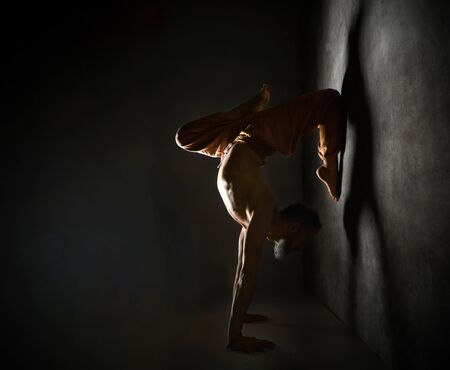 Gray-haired, barefoot, elderly yogi man with naked torso, in brown pants and bracelets is practicing...