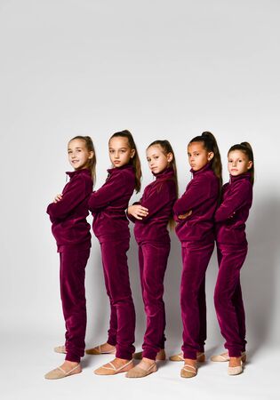 Group of young smiling girls gymnasts in dark red velvet sport costumes standing and posing over white background. Rhytmhic gimnastics beauty and team sport cocneptの写真素材