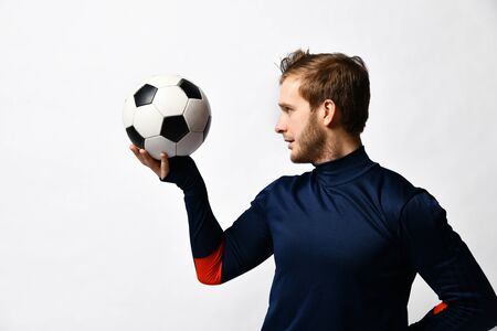professional soccer player in a blue tracksuit is about to throw the ball, holds it with one hand, presenting sideways, isolated on a white studio background. The concept of sport, balance and agility.の写真素材