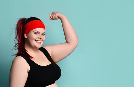 Portrait of a young fat ginger model in a red headband, black top. She shows her strength in the arms of her biceps. On a blue backgroundの写真素材