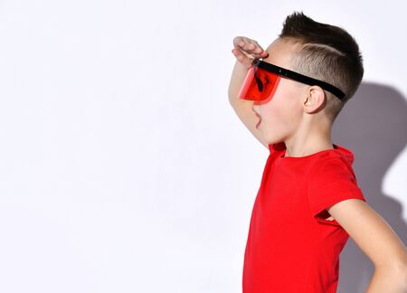 teenage child in huge sunglasses with a protective visor, a red T-shirt and black bracelets. He looks surprised forward, presenting sideways, isolated on white.の写真素材