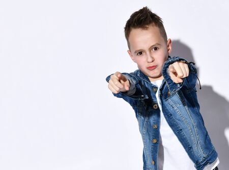 Teenager in t-shirt, blue denim jacket and black bracelet. He is pointing at you while posing isolated on white studio background. Childhood, fashion, advertising. Close up, copy spaceの写真素材