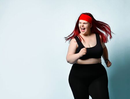 Close up portrait of young attractive plus-size model with flowing red hair, squinted eyes and naughty toothy smile on blue background. Fitness, diet, body positive, healthy way of life. Copy spaceの写真素材