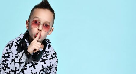 teenage child with headphones on neck, in sunglasses, stylish hoodie and black bracelet. He is...