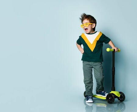 Joyful boy wearing a colorful T-shirt, yellow glasses, gray jeans, sneakers. The guy stands near his...