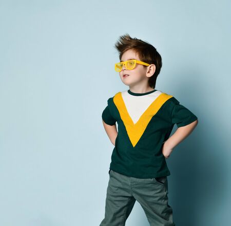 Little fashionable man in funny striped glasses posing on a blue studio background.