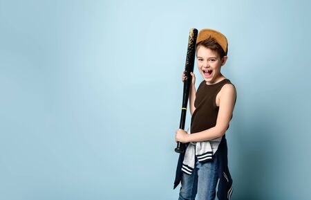 Teenage child in cap and casual clothes. He is holding black shabby baseball bat or club and...