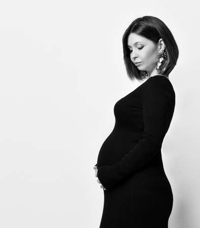 pregnant woman in black tight dress and massive earrings. She put hand on her belly, posing sideways...