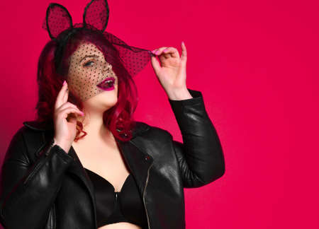 Cute sexy plus size brunette with black bunny ears in leather jacket and underwear posing on red background.の写真素材