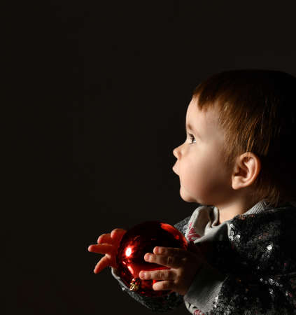 Portrait of lovely baby playing with Christmas ball against black background