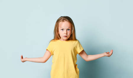 Adorable blonde kid in yellow t-shirt. She spreads her hands wide apart like holding something and...
