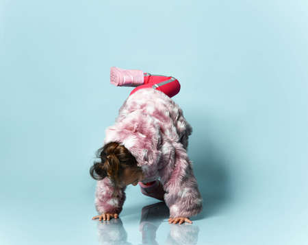 Little girl with a bun hairstyle, dressed in a pink fur coat, trousers and boots. She is fooling...