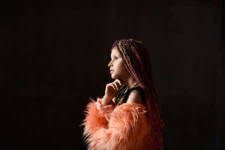 Cropped side shot of a pensive little girl with pigtails posing in the dark wearing a black...