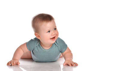 Portrait of a baby boy toddler boy with dark blue eyes wearing a striped turquoise bodysuit. The child lies on his stomach and tries to cry, looking to the side on a white background.の写真素材