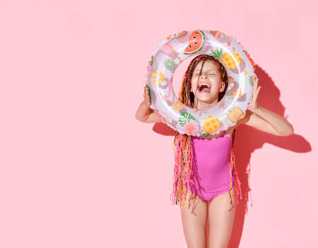 Cute girl with multicolored afro bunches in bright rose swimsuit laughing happily holding rubber...