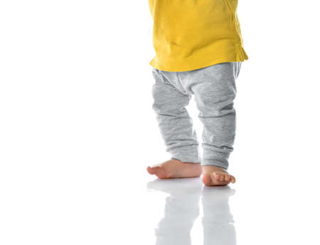 Little baby barefoot leg cropped view. Kid stepping taking balance. Toddler child first step. Time to walk. Children development and growth. Studio portrait on white wall backgroundの写真素材